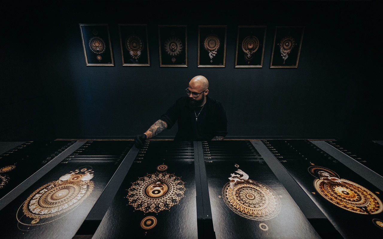 Billelis in a dark room with a print run of his gold-on-black work laid out on tables
