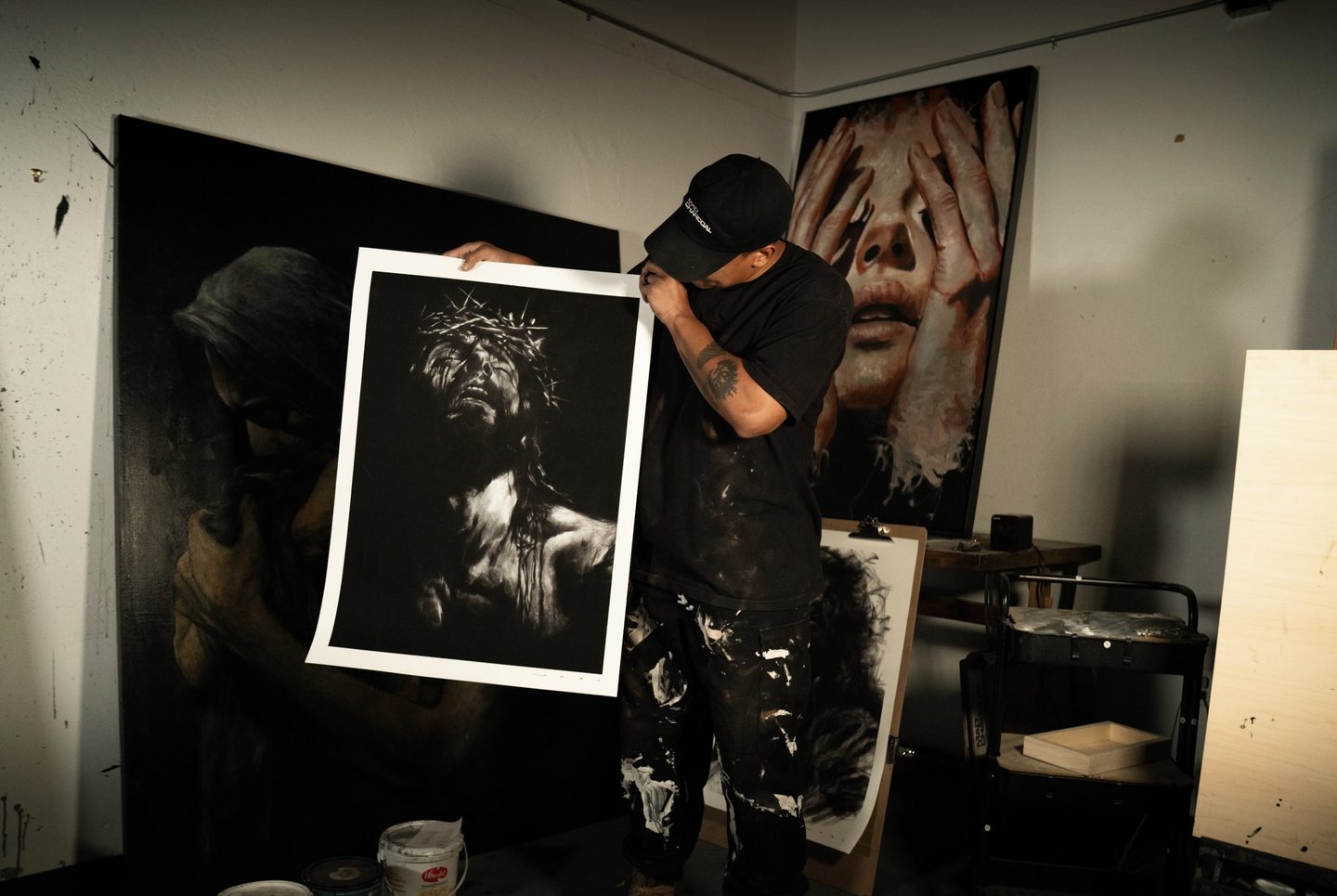 Josh Hernandez in his studio, holding a print of one of his charcoal drawings