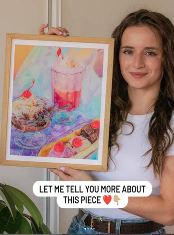 An artist showing a framed print to her audience — artwork © Lily-Rose Burgess