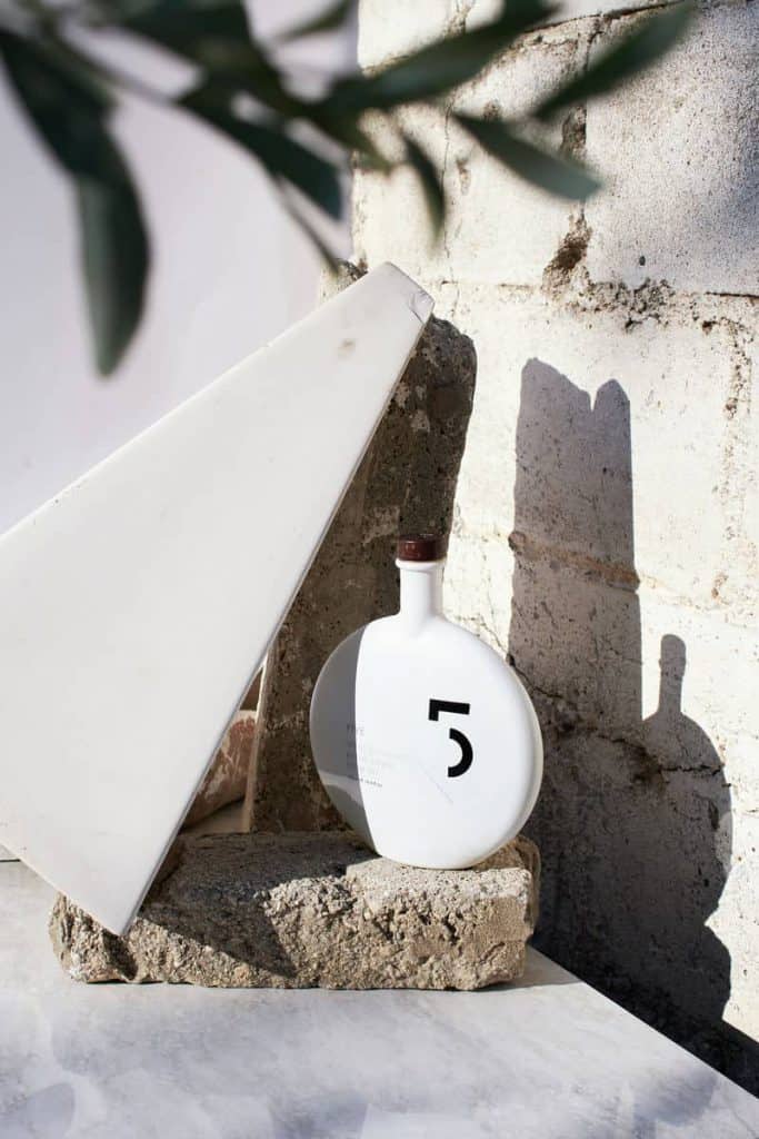 A bottle of oil photographed outdoors against a stone wall in natural light by Greece-based product photographer Mika Michopoulou